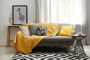 Canapé avec plaid jaune et coussins.