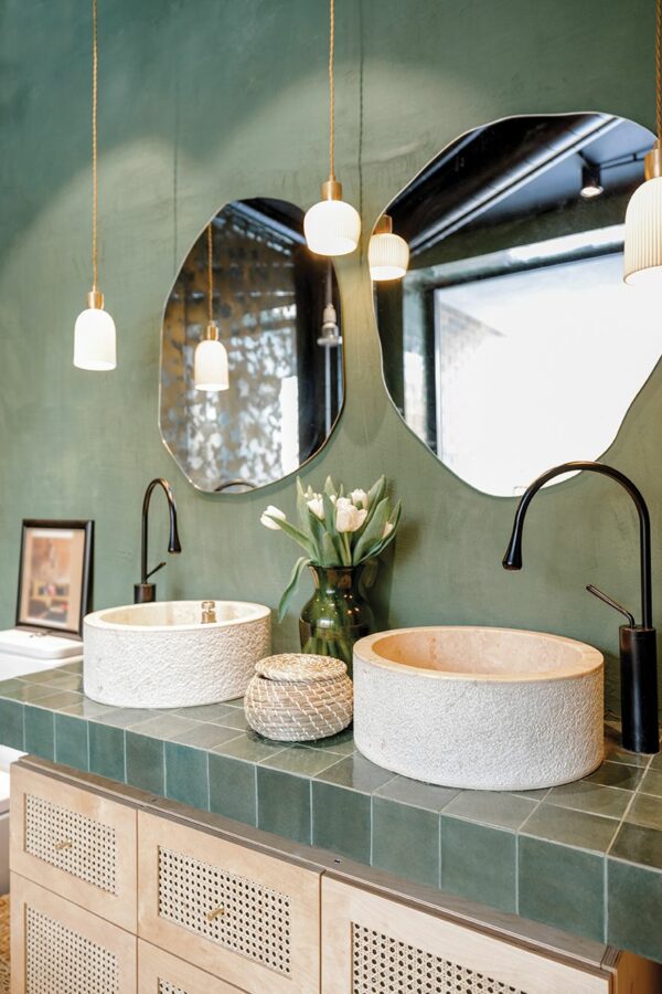 Bathroom interior with stone wash basins, modern faucets, irregularly shaped mirrors and wooden rattan commode in green and beige tones in natural boho style